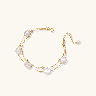 Delicate multi-layered gold-plated bracelet with irregular baroque pearls and freshwater pearls on cream background.