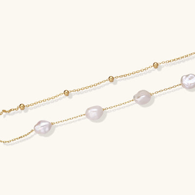 Delicate multi-layered gold-plated bracelet with irregular baroque pearls and freshwater pearls on cream background.