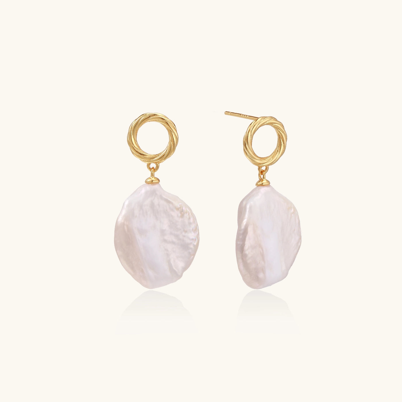 Gold-plated twisted stud earrings with large blush baroque pearls hanging elegantly on white background.