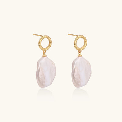 Gold-plated twisted stud earrings with large blush baroque pearls hanging elegantly on white background.