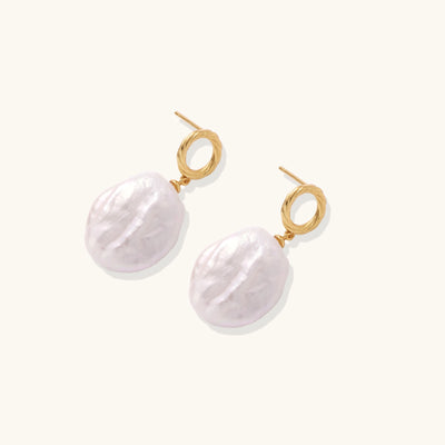 Gold-plated twisted stud earrings with large blush baroque pearls hanging elegantly on white background.