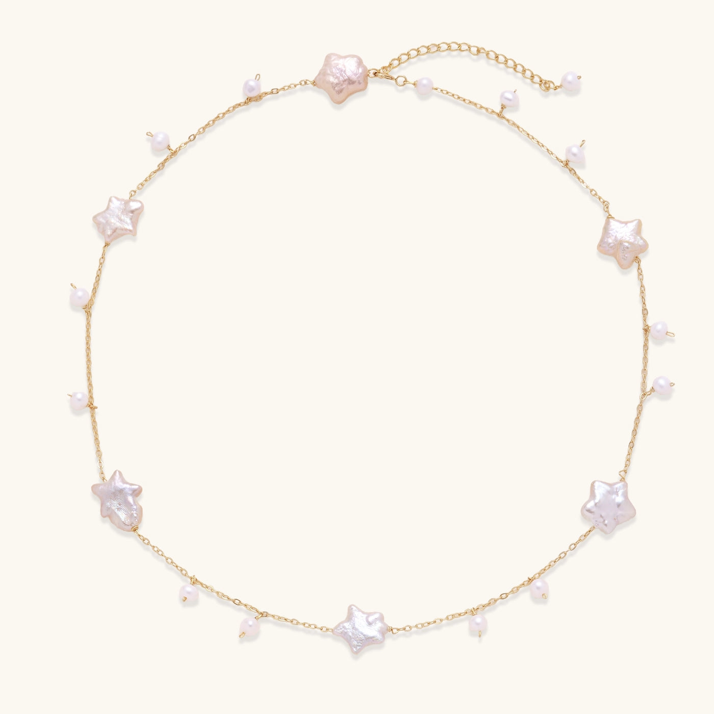 Delicate gold chain necklace with star-shaped baroque pearls and small freshwater pearls on cream background.