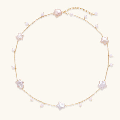 Delicate gold chain necklace with star-shaped baroque pearls and small freshwater pearls on cream background.