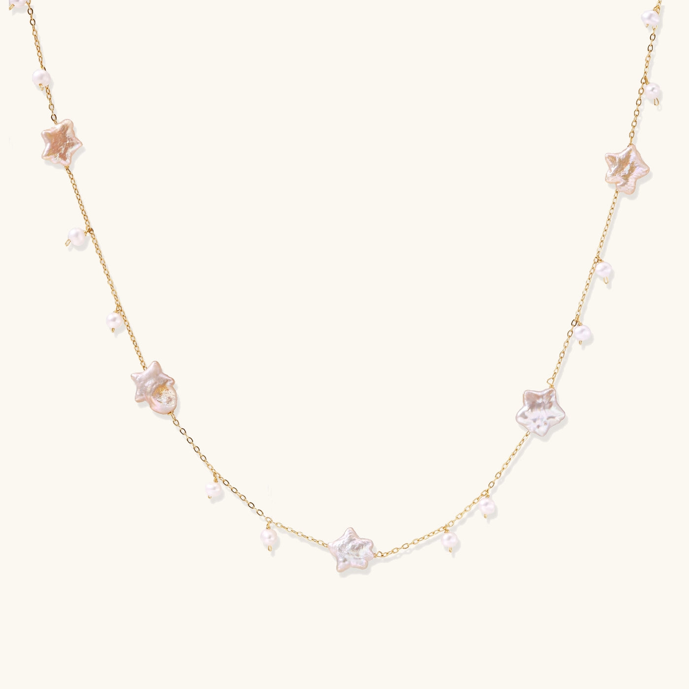 Delicate gold chain necklace with star-shaped baroque pearls and small freshwater pearls on cream background.