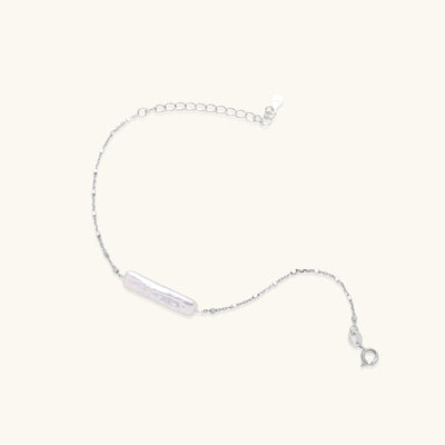 Delicate sterling silver chain bracelet with an organic white baroque pearl centerpiece on neutral background