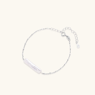 Delicate sterling silver chain bracelet with an organic white baroque pearl centerpiece on neutral background