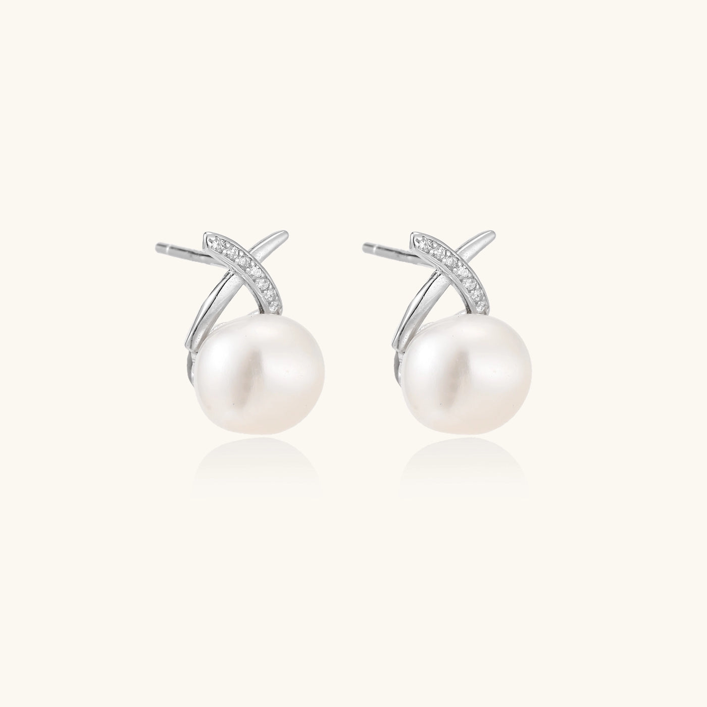Sterling silver cross-shaped stud earrings with round freshwater pearls dangling below on white background.