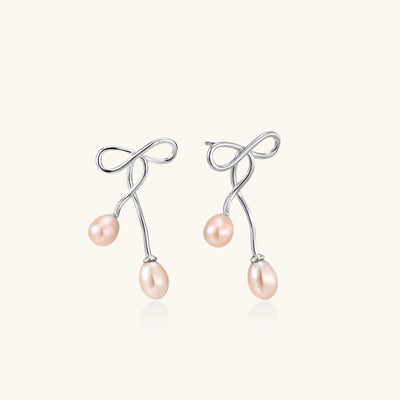 Delicate sterling silver wire earrings with organic bow shapes and two pink freshwater pearls on white background