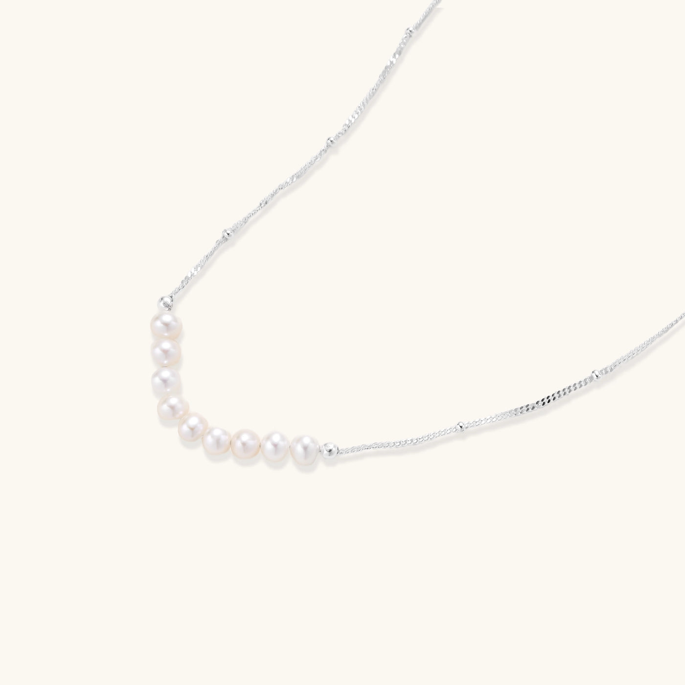 Delicate sterling silver chain with small white freshwater pearls arranged asymmetrically on white background.