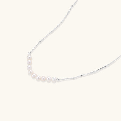 Delicate sterling silver chain with small white freshwater pearls arranged asymmetrically on white background.