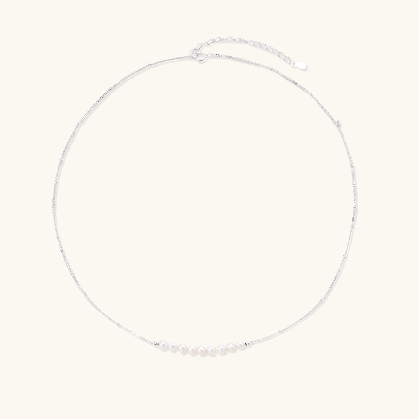 Delicate sterling silver chain with small white freshwater pearls arranged asymmetrically on white background.