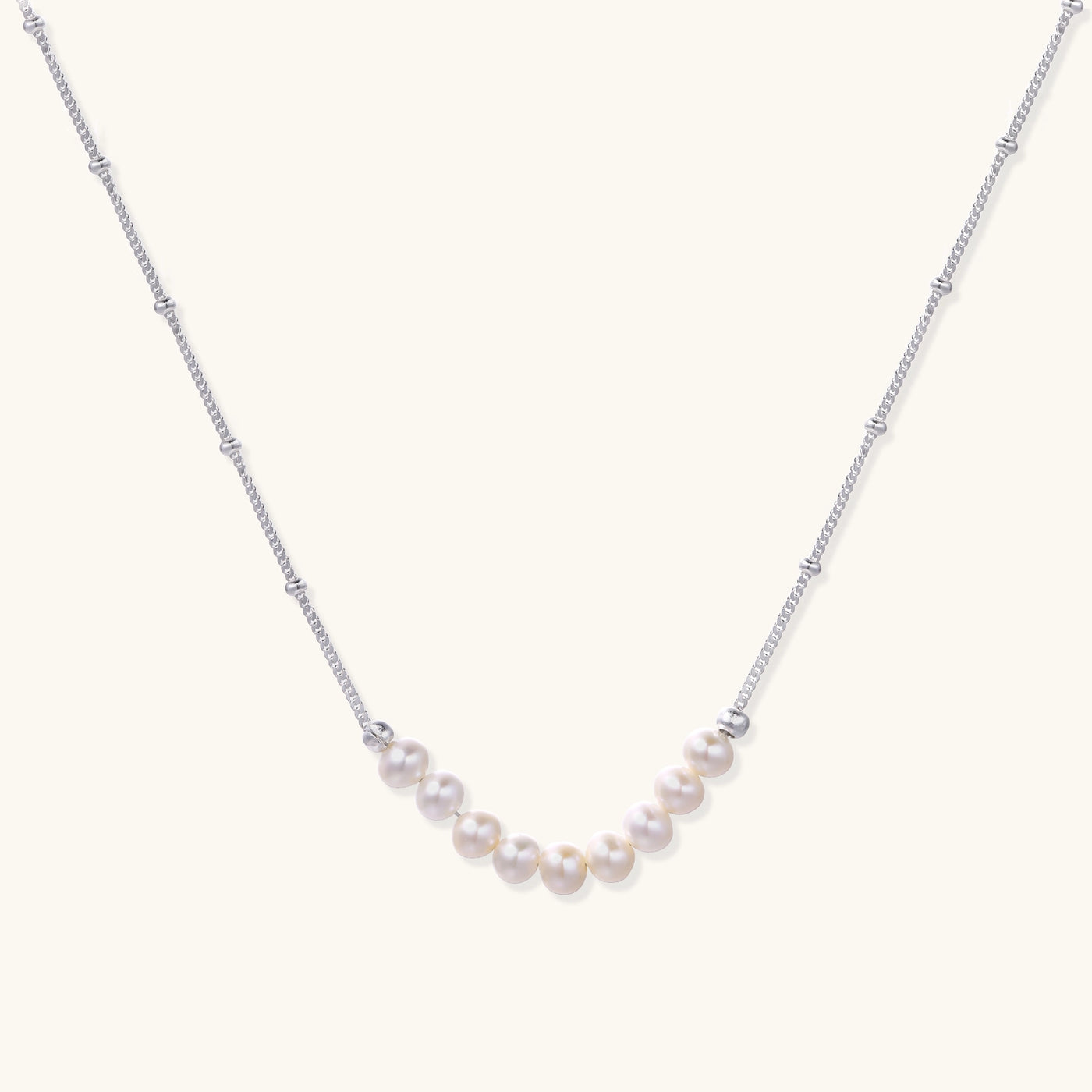 Delicate sterling silver chain with small white freshwater pearls arranged asymmetrically on white background.