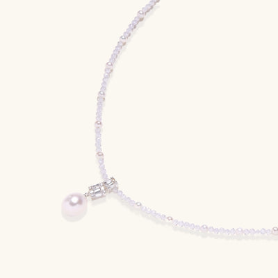 Delicate beaded necklace with lavender crystals, white pearls, and crystal pendant with pearl drop on white background.