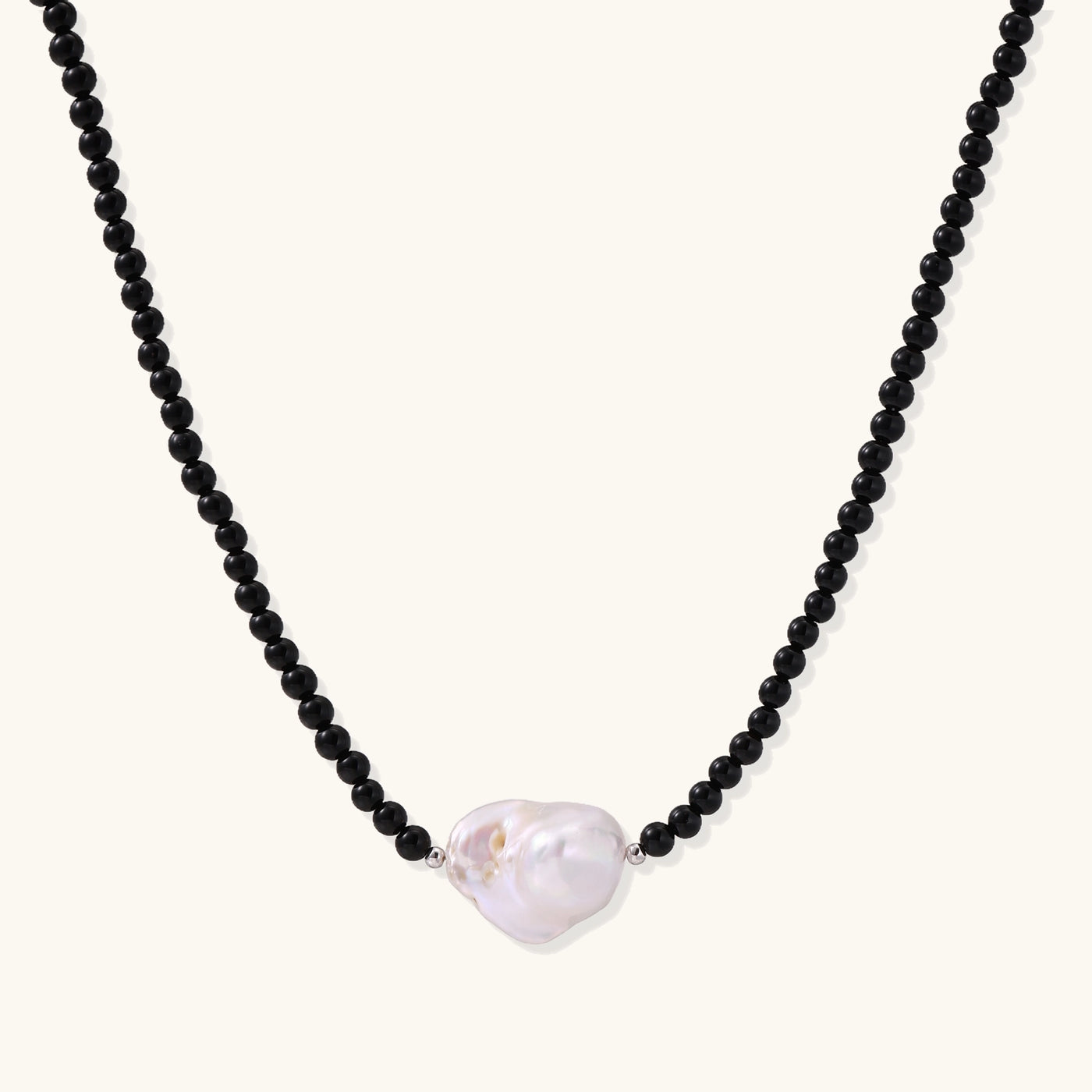 Elegant necklace with black agate beads and iridescent baroque freshwater pearl centerpiece on white background.