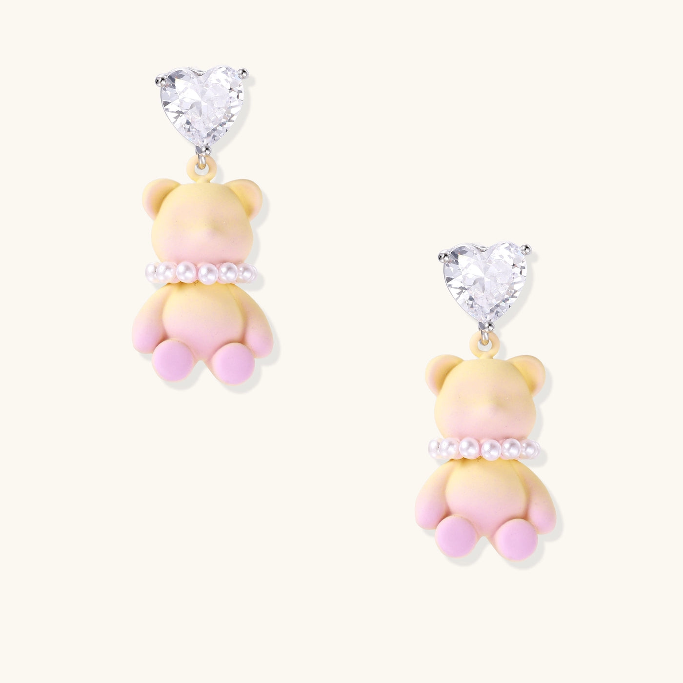 Cute teddy bear earrings with heart-shaped crystals, gold plating, and white pearl accents in pink and blue variants