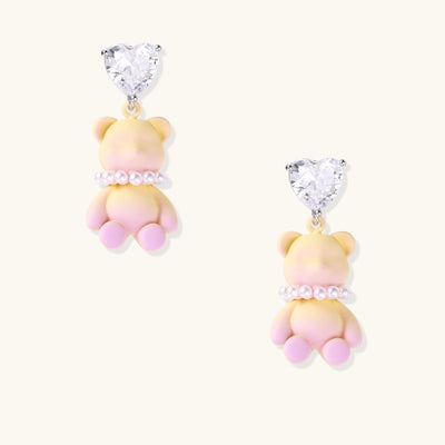 Cute teddy bear earrings with heart-shaped crystals, gold plating, and white pearl accents in pink and blue variants