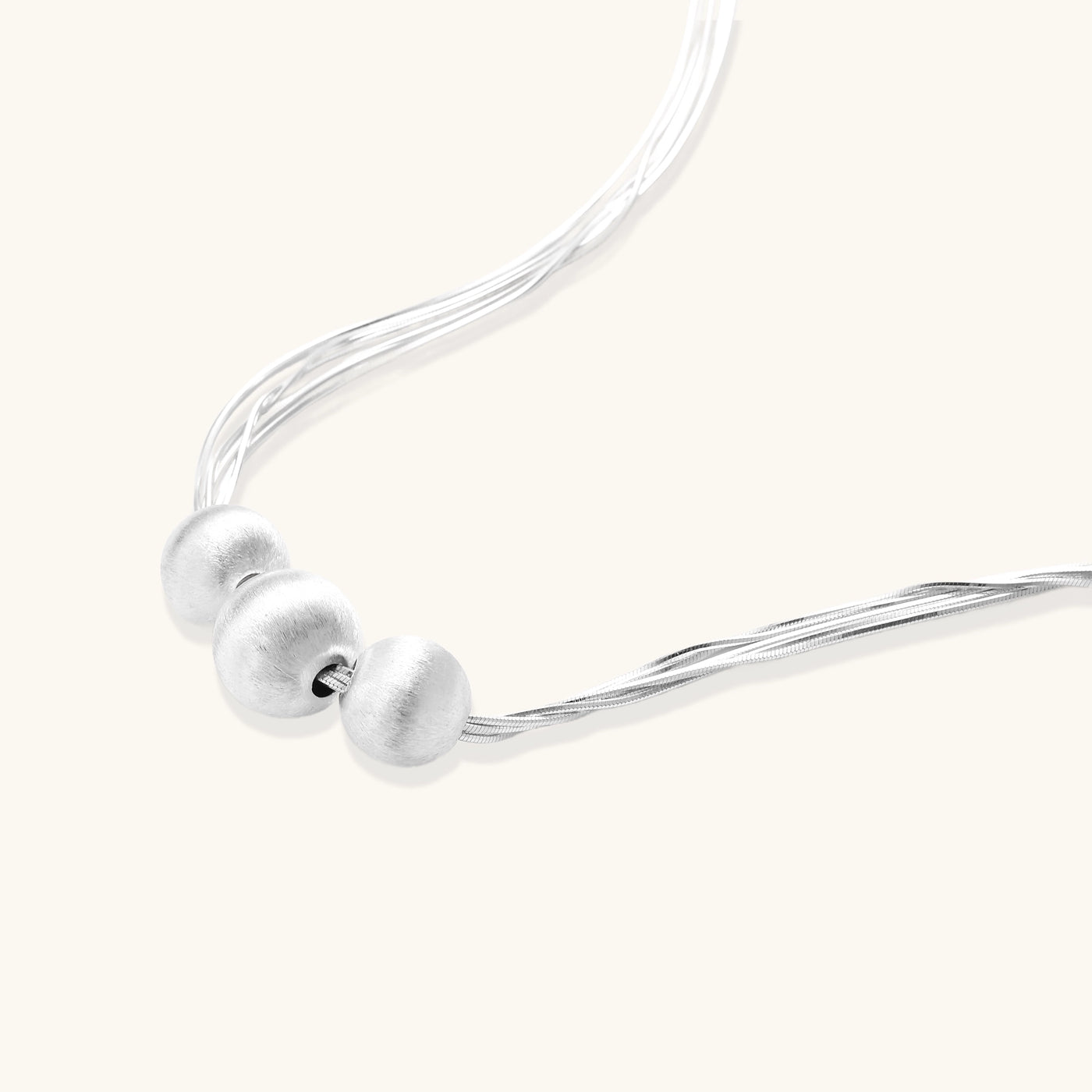 Multi-strand sterling silver necklace with three polished round beads clustered at center on white background.