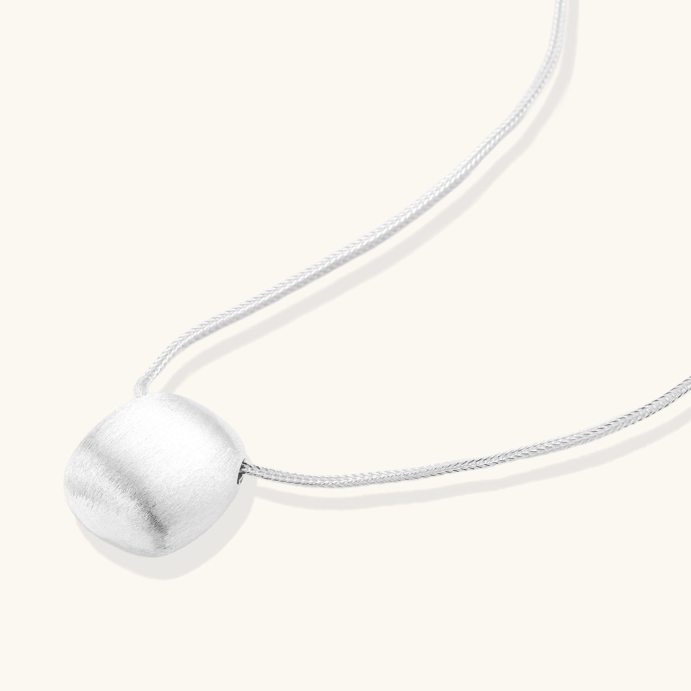 Minimalist sterling silver necklace with brushed square pendant on adjustable chain against white background.