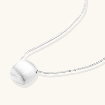 Minimalist sterling silver necklace with brushed square pendant on adjustable chain against white background.