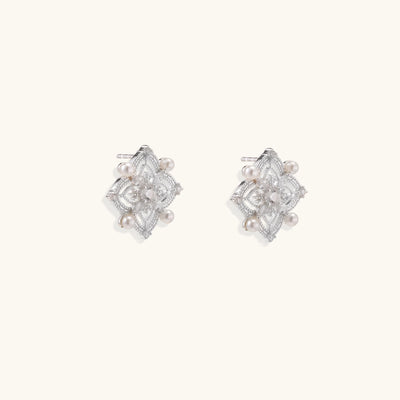Detailed view of sterling silver stud earrings with geometric filigree design and small freshwater pearls on white background.