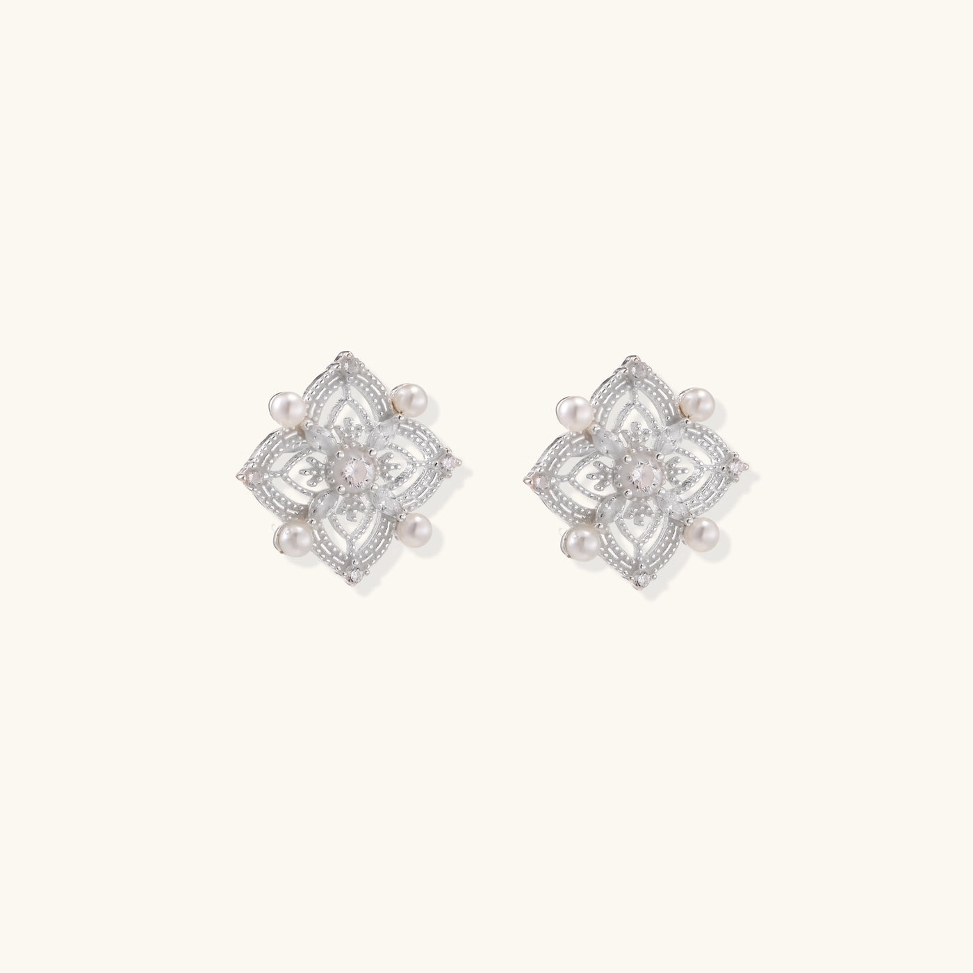 Detailed view of sterling silver stud earrings with geometric filigree design and small freshwater pearls on white background.