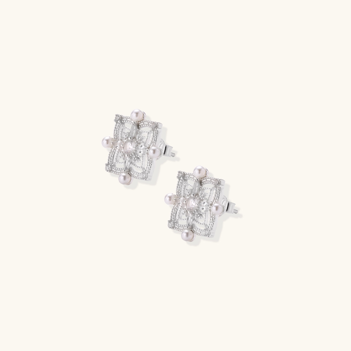 Detailed view of sterling silver stud earrings with geometric filigree design and small freshwater pearls on white background.