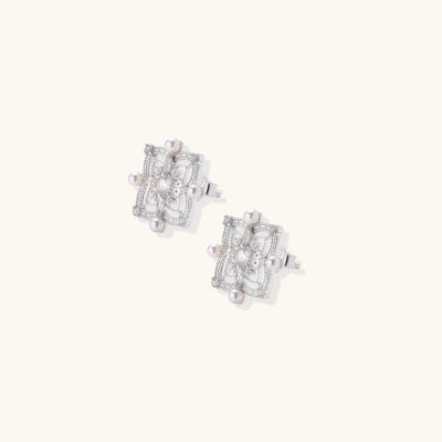 Detailed view of sterling silver stud earrings with geometric filigree design and small freshwater pearls on white background.