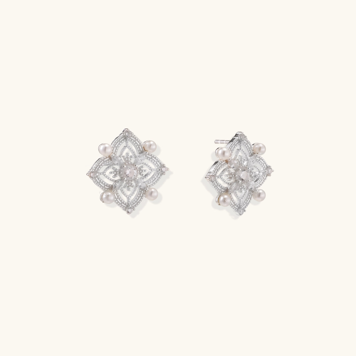 Detailed view of sterling silver stud earrings with geometric filigree design and small freshwater pearls on white background.