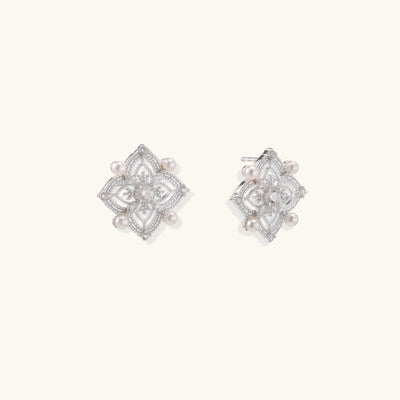 Detailed view of sterling silver stud earrings with geometric filigree design and small freshwater pearls on white background.