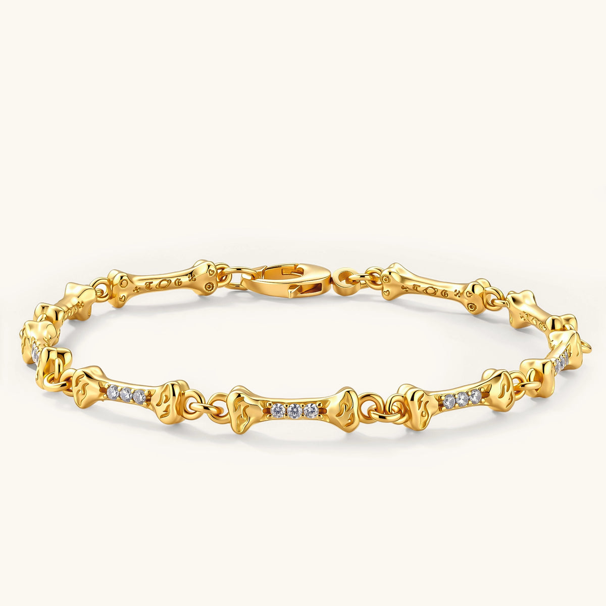 Gold-plated sterling silver bracelet with bone-shaped links, embedded CZ stones, and lobster clasp on light background.
